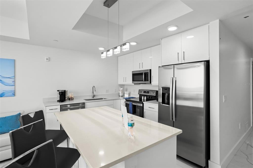 A modern kitchen features white cabinetry, stainless steel appliances, and a central quartz island — 11500 GULF BOULEVARD UNIT 202, ST PETERSBURG, FL