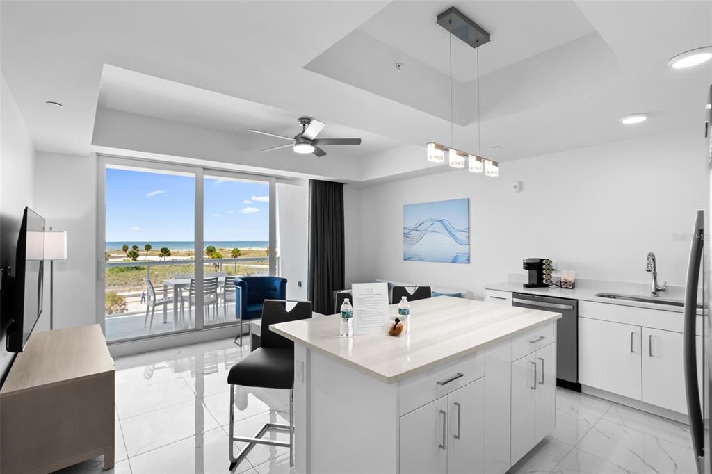 A modern kitchen with a white island and tile floors overlooks a balcony and beach — 11500 GULF BOULEVARD UNIT 202, ST PETERSBURG, FL