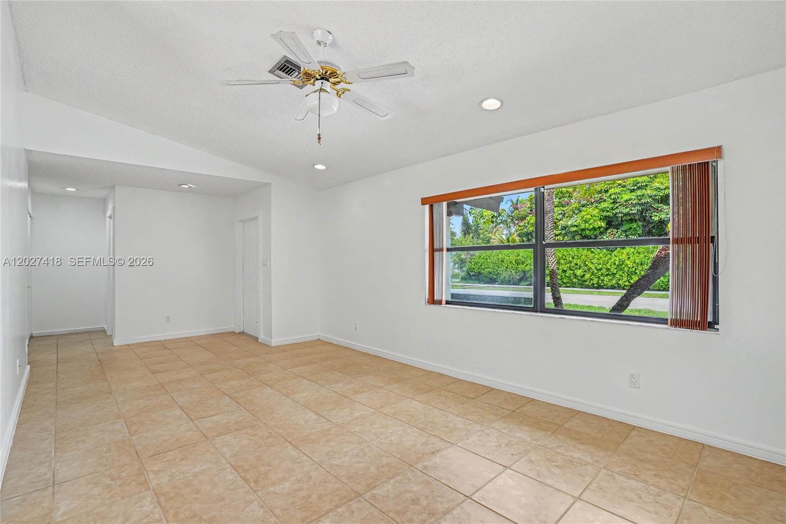 An empty room features white walls, tan tile flooring, a ceiling fan, and a large window — 10711 SW 116th Ave, Miami FL 33176, MIAMI, FL