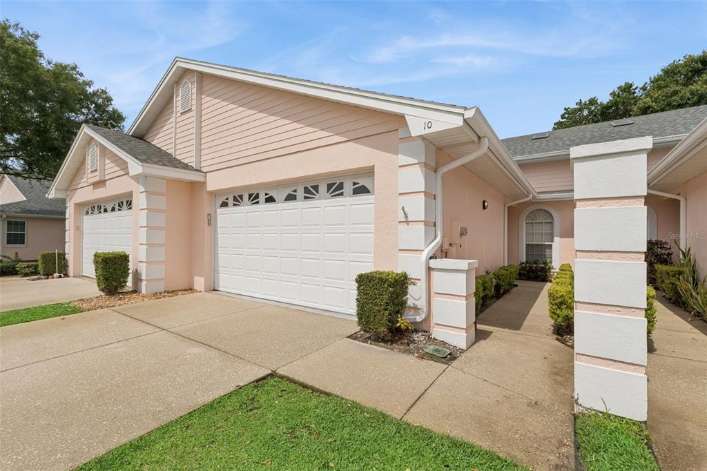 A peach-colored house with a two-car garage and a concrete walkway leading to the entrance — 10 ENCLAVE DRIVE, WINTER HAVEN, FL