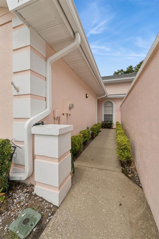 A narrow concrete walkway runs between two pink stucco walls alongside a house exterior — 10 ENCLAVE DRIVE, WINTER HAVEN, FL