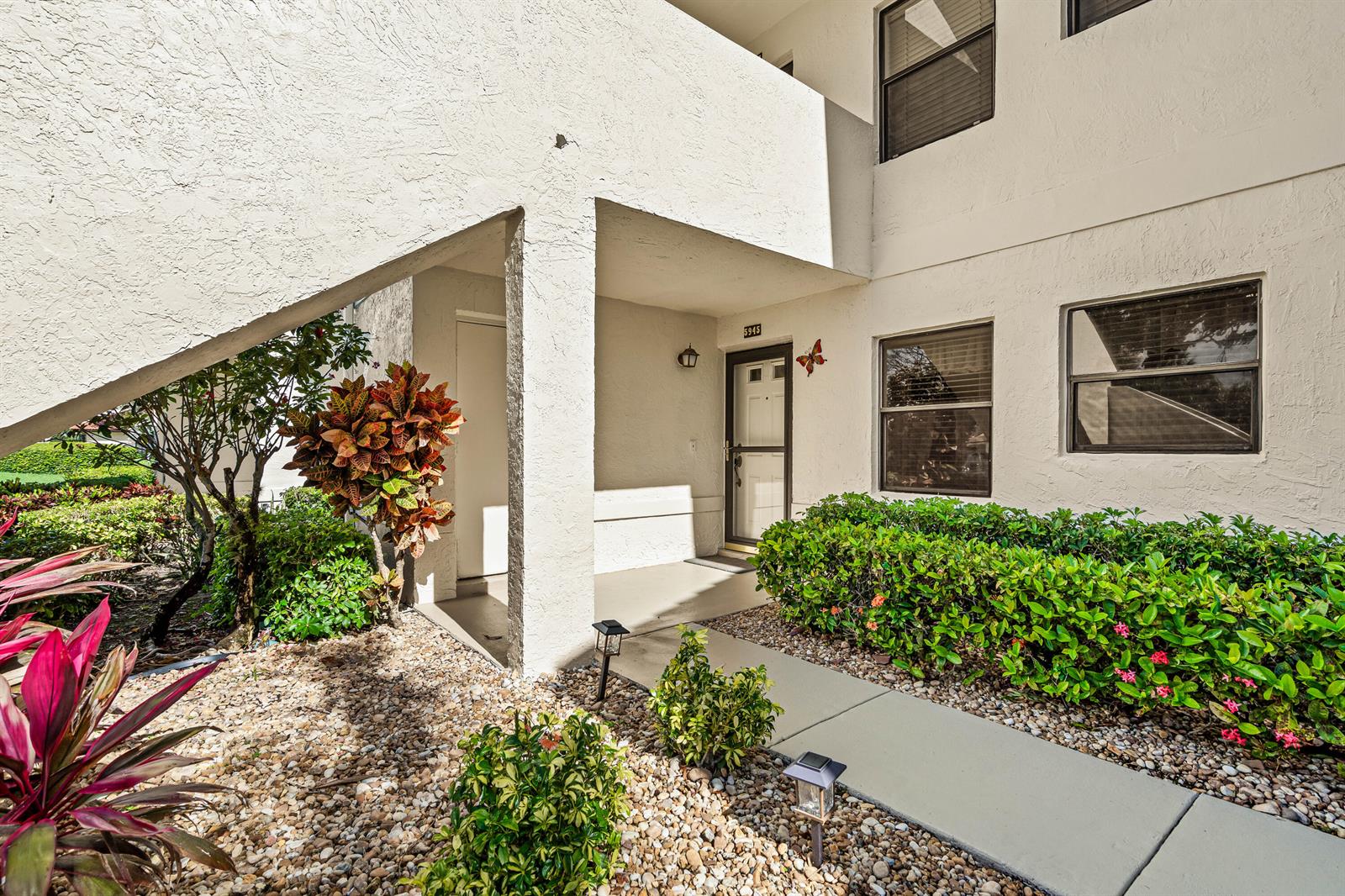 The exterior of a ground-floor apartment features a concrete walkway, landscaping, and a covered entrance — 5945 Parkwalk Drive, Boynton Beach FL 33472, BOYNTON BEACH, FL