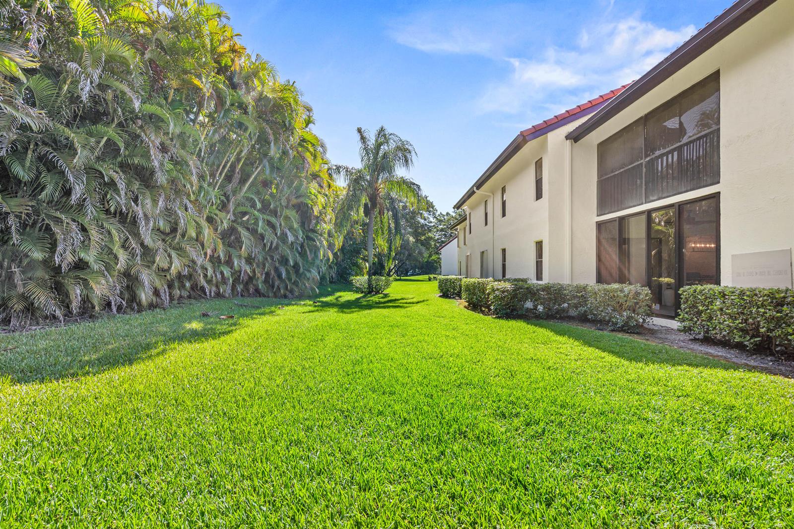 A view of a grassy backyard next to a two-story building with a screened balcony — 5945 Parkwalk Drive, Boynton Beach FL 33472, BOYNTON BEACH, FL
