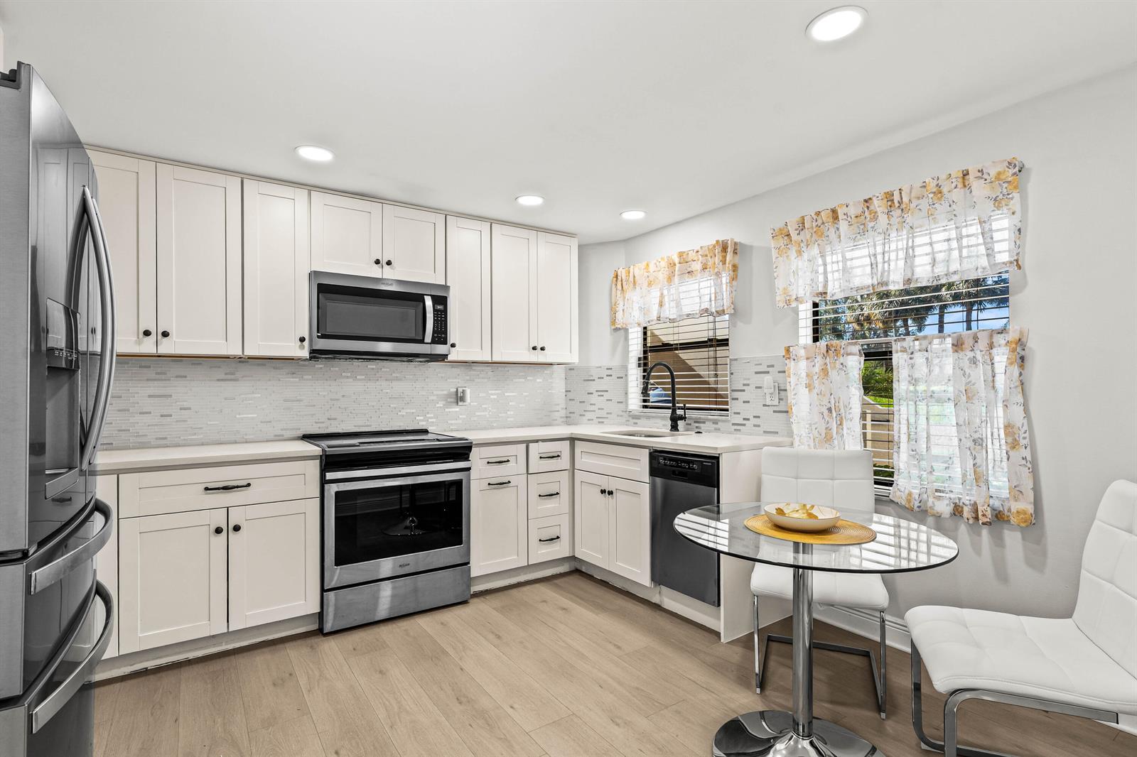 A kitchen features white cabinets, stainless steel appliances, a glass dining table, and light flooring — 5945 Parkwalk Drive, Boynton Beach FL 33472, BOYNTON BEACH, FL