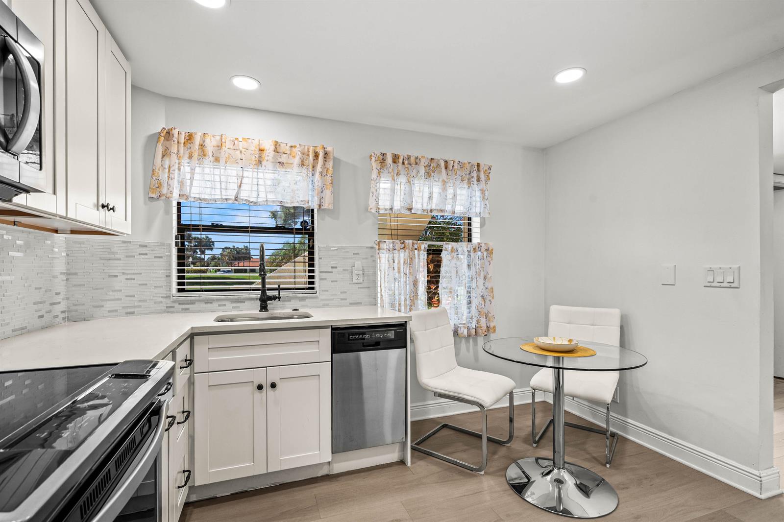 A kitchen features white cabinets, stainless steel appliances, a glass dining table, and two chairs — 5945 Parkwalk Drive, Boynton Beach FL 33472, BOYNTON BEACH, FL