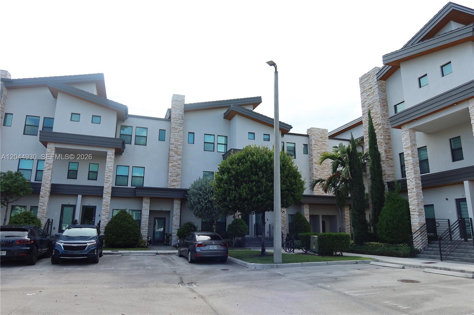 A multi-story residential building features light-colored stucco, stone accents, and a paved parking area — 10467 NW 82nd St # 16, Doral FL 33178, DORAL, FL