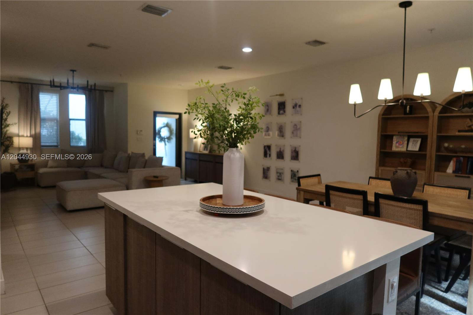 A kitchen island with a white countertop sits in the foreground of an open-concept living area — 10467 NW 82nd St # 16, Doral FL 33178, DORAL, FL