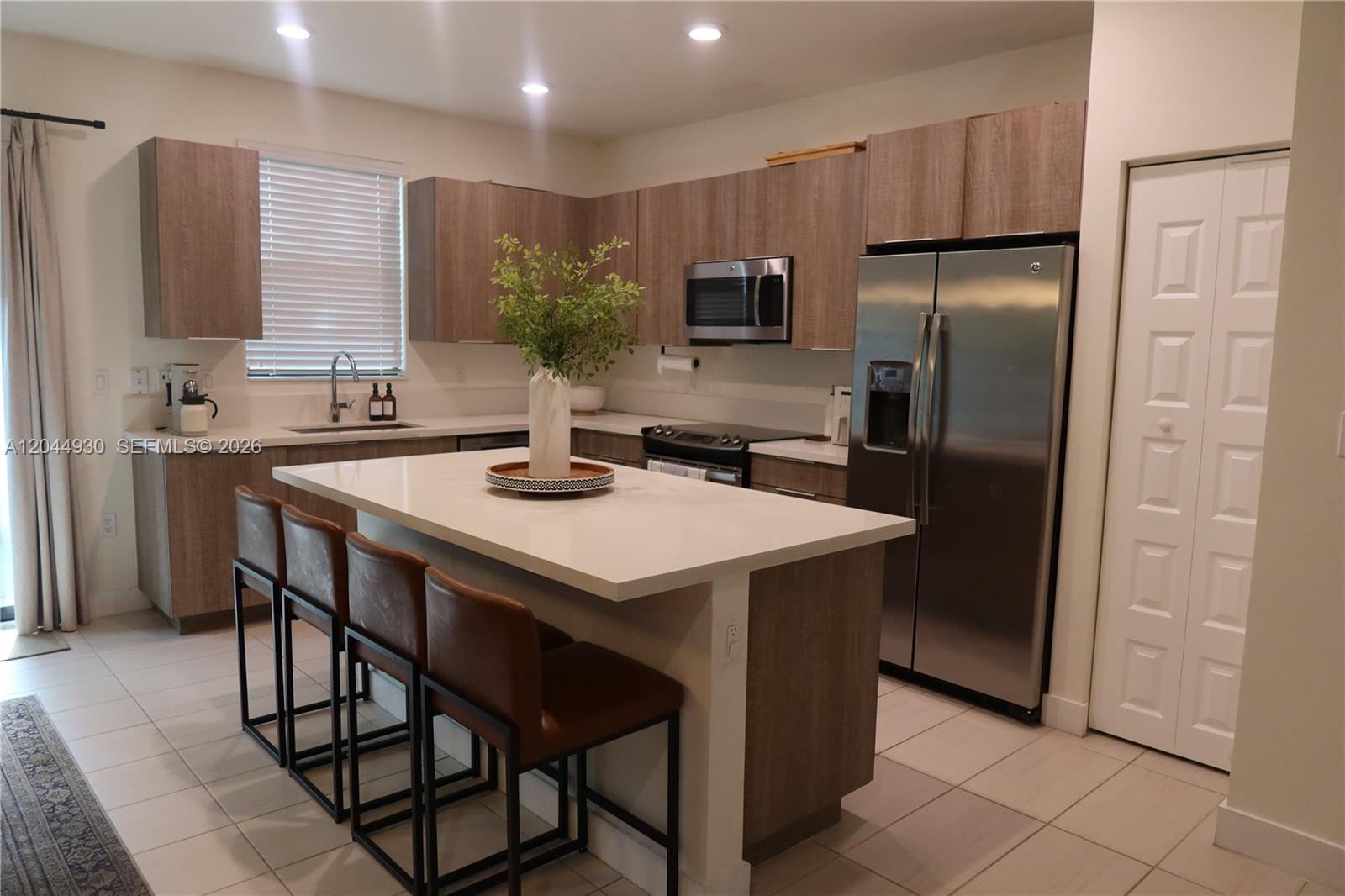 A modern kitchen features wood-grain cabinets, stainless steel appliances, and a large white island — 10467 NW 82nd St # 16, Doral FL 33178, DORAL, FL