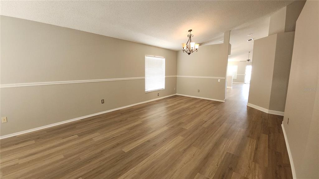 An empty room with light wood-look flooring, beige walls, chair rail molding, and a chandelier — 12507 MIDPOINTE DRIVE, RIVERVIEW, FL