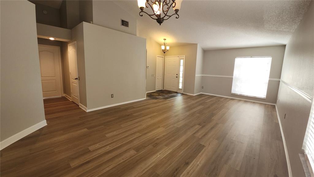 An empty living room with light gray walls, wood-look flooring, and a vaulted ceiling — 12507 MIDPOINTE DRIVE, RIVERVIEW, FL