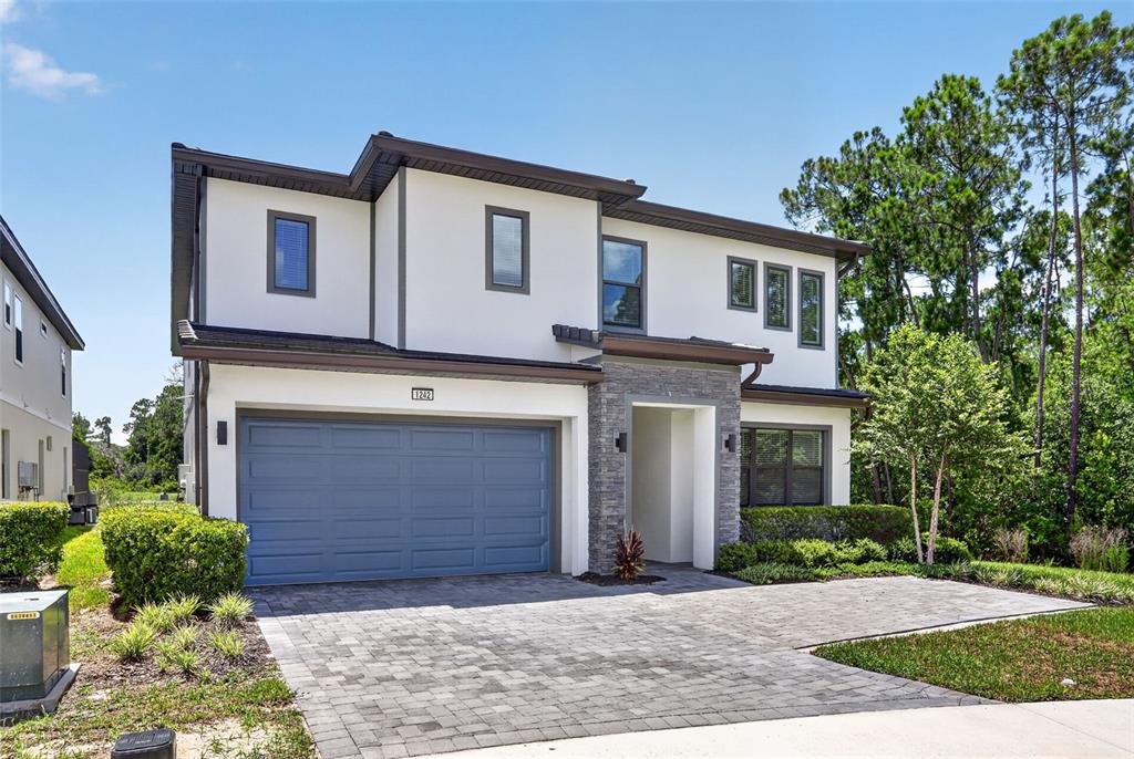 A two-story house with a blue garage door, stone accents, and a paved driveway — 1242 BUTTERFLY ORCHID ROAD, DAVENPORT, FL