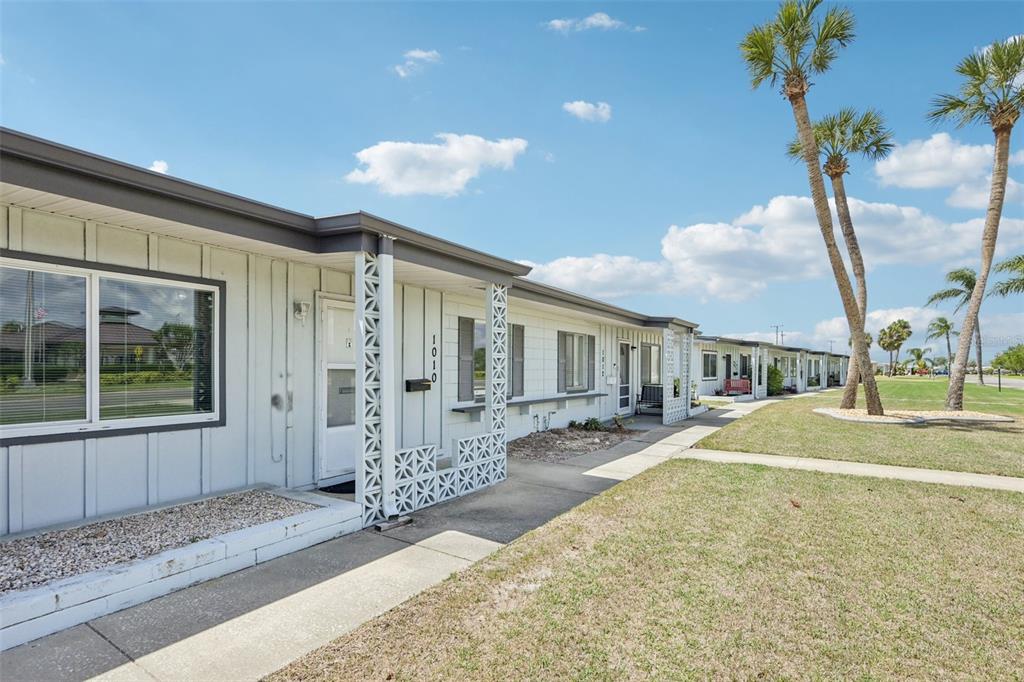 A row of single-story residential units with white siding and decorative concrete block privacy screens — 1010 N PEBBLE BEACH BOULEVARD, SUN CITY CENTER, FL