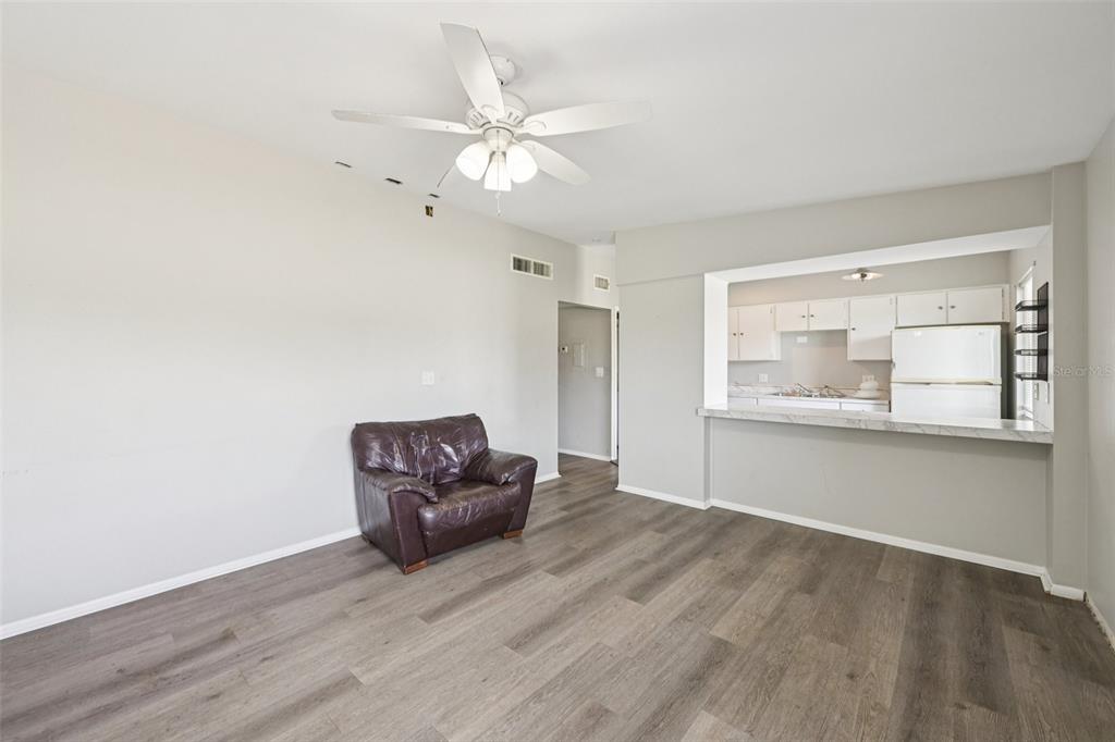 A living room with gray wood-look flooring, a ceiling fan, and an open kitchen pass-through — 1010 N PEBBLE BEACH BOULEVARD, SUN CITY CENTER, FL
