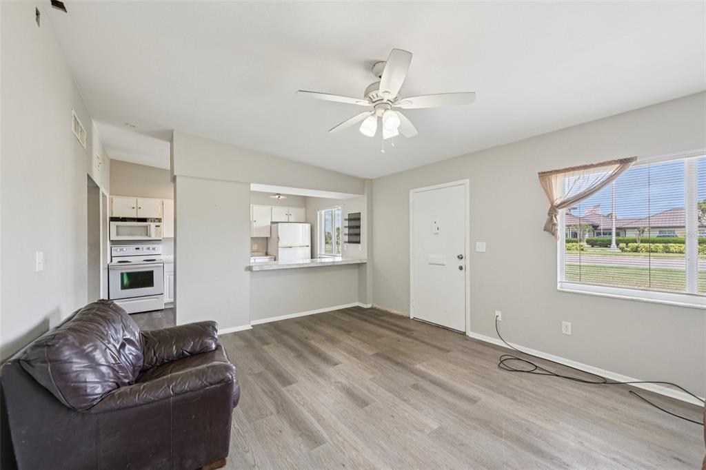 A living room with gray wood-look flooring, a ceiling fan, and an open kitchen pass-through — 1010 N PEBBLE BEACH BOULEVARD, SUN CITY CENTER, FL