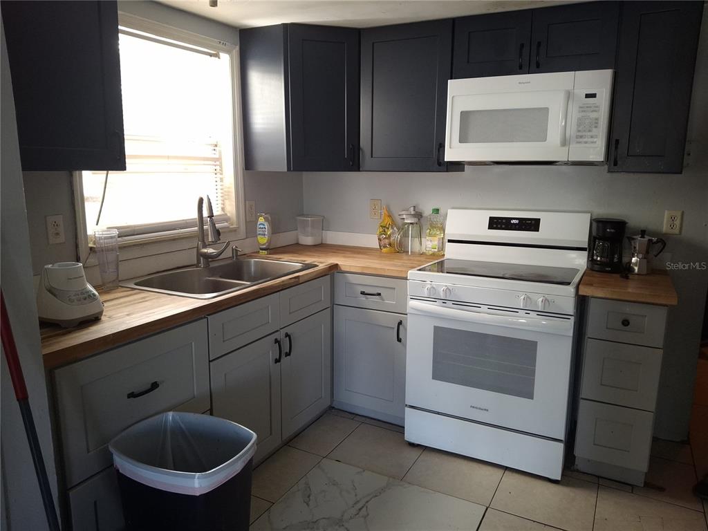 A kitchen features dark upper cabinets, light gray lower cabinets, and wood countertops — 1127 AUBURN STREET, CLEARWATER, FL