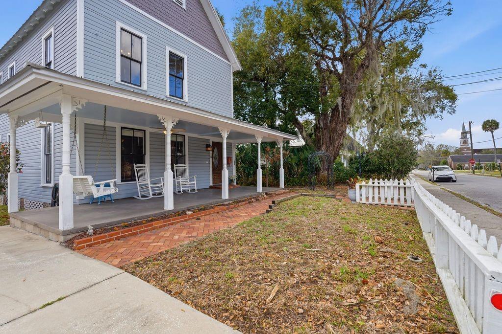 A blue two-story house features a wrap-around porch with a swing and white rocking chairs — 720 SE 3RD STREET, OCALA, FL