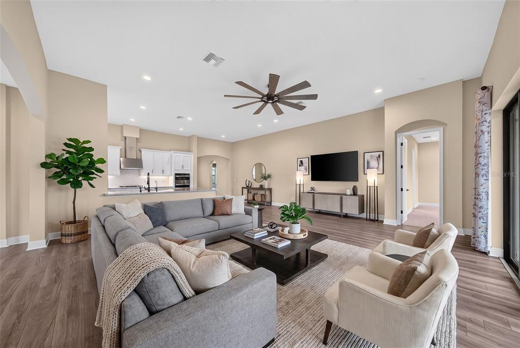 A spacious open-concept living room features a gray sectional, two armchairs, and a modern kitchen — 12627 WHEATGRASS COURT, PARRISH, FL