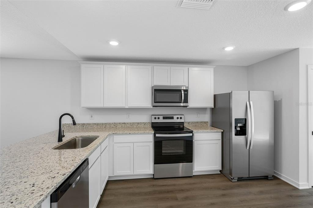 A kitchen features white cabinets, granite countertops, stainless steel appliances, and wood-look flooring — 7172 CANOPY LANE, LAKELAND, FL