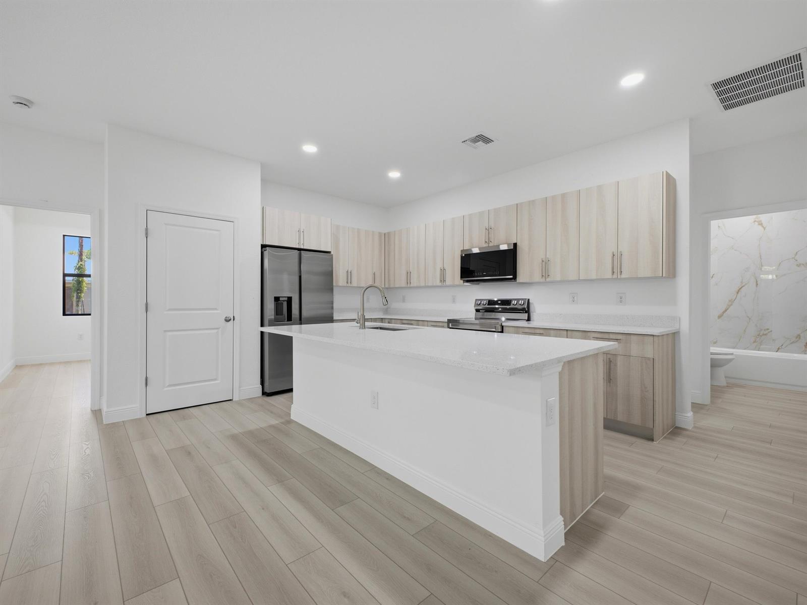 A modern kitchen features light wood cabinets, white countertops, a central island, and stainless appliances — 8010 Sandalwood Lane, FL 33935, FL