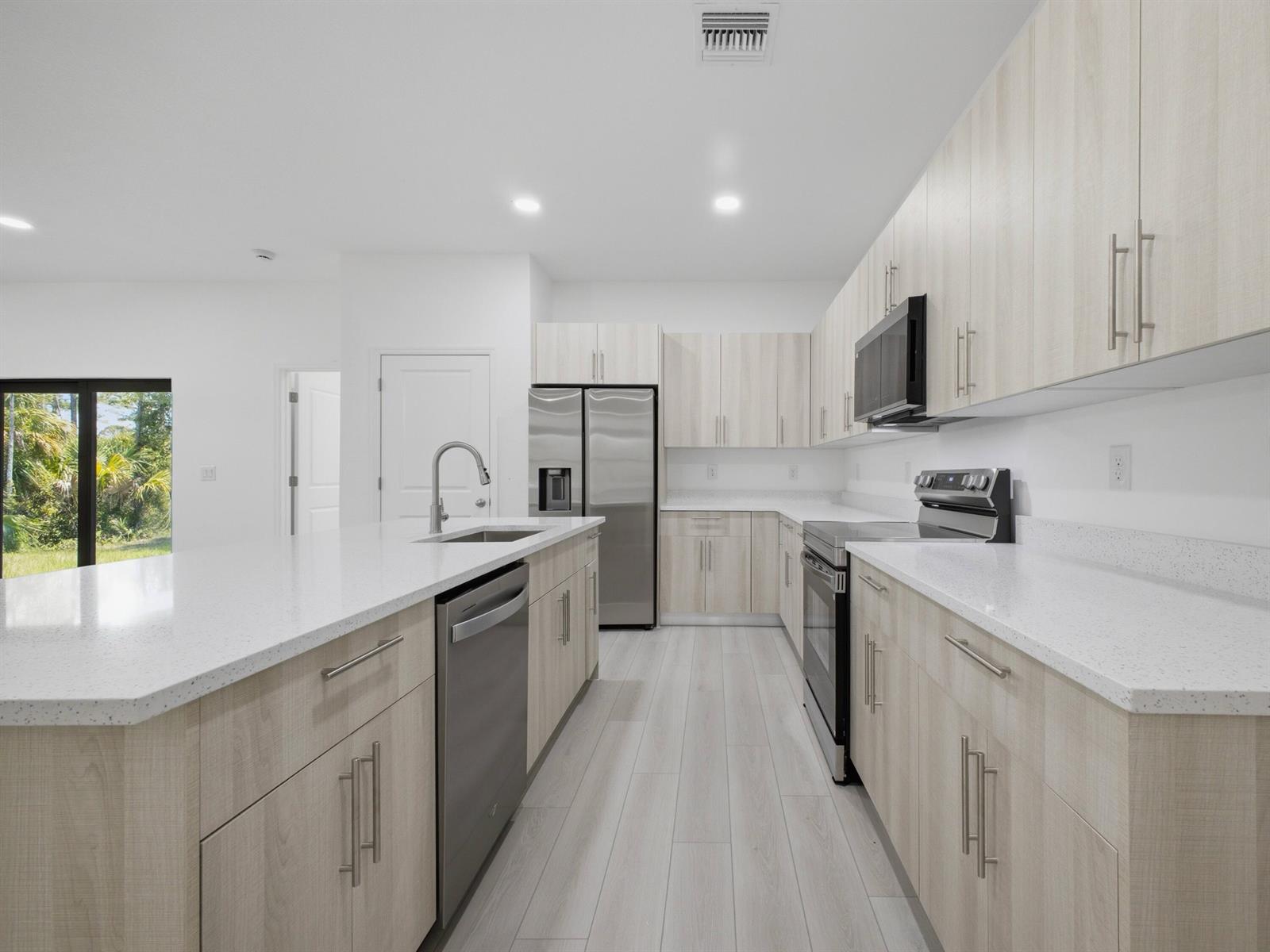 A modern kitchen features light wood cabinets, white countertops, stainless steel appliances, and tile flooring — 8010 Sandalwood Lane, FL 33935, FL