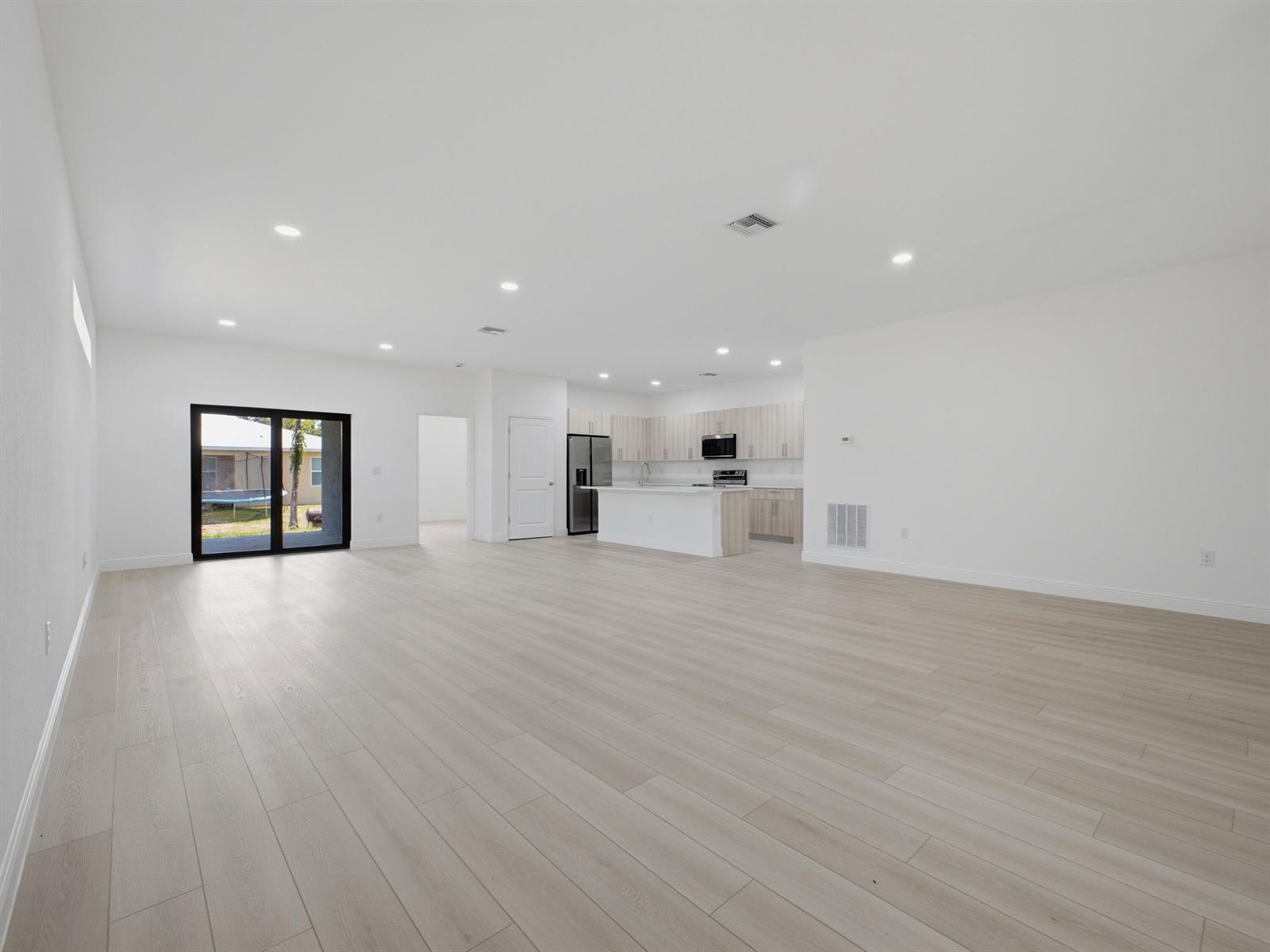 An open-concept living area features light wood-look flooring, white walls, and a modern kitchen — 8010 Sandalwood Lane, FL 33935, FL