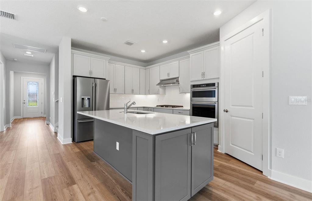 A modern kitchen features white cabinetry, a gray island, stainless steel appliances, and wood flooring — 13504 CANYON RIDGE ROAD, SPRING HILL, FL