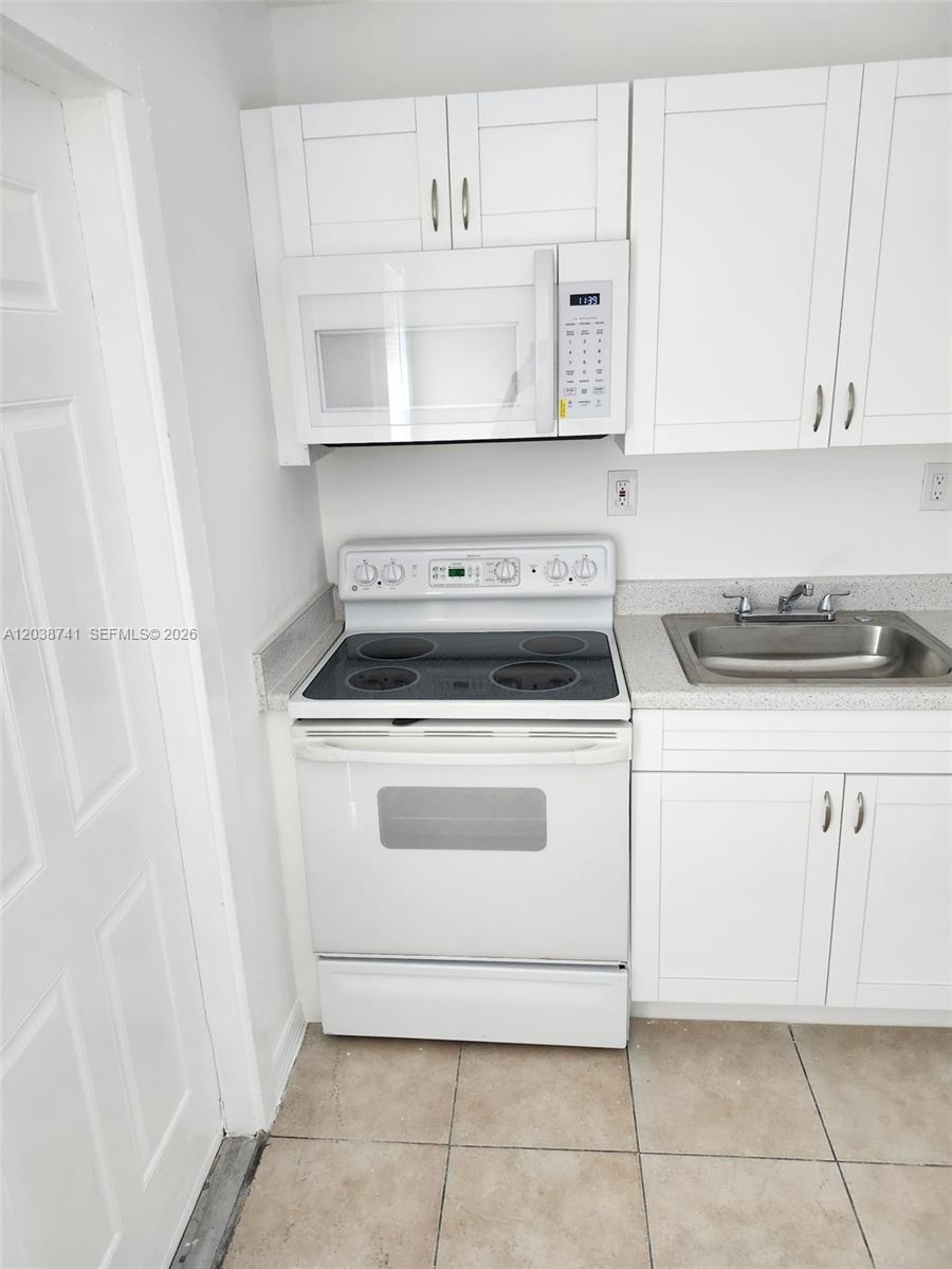 A small kitchen features white cabinets, a white electric stove, and a stainless steel sink — 726 21st St # 3, West Palm Beach FL 33407, WEST PALM BEACH, FL