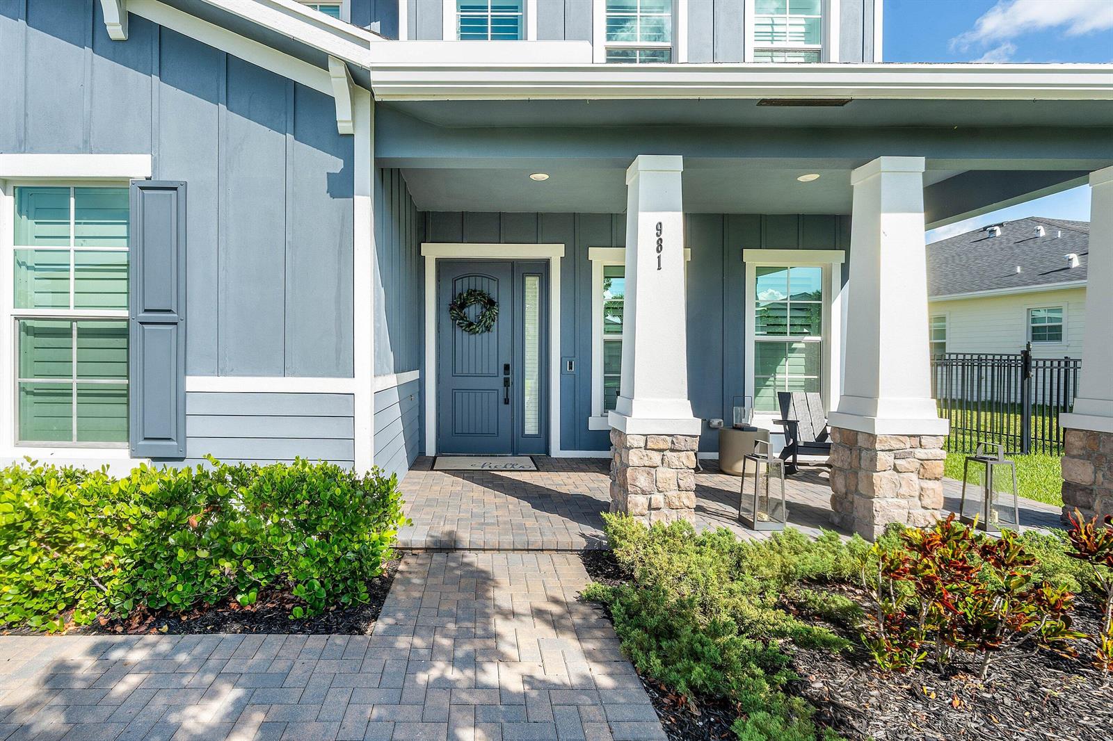 The exterior of a blue house features a stone-based porch, a front door, and landscaping — 981 Castaway Court, Loxahatchee FL 33470, LOXAHATCHEE, FL
