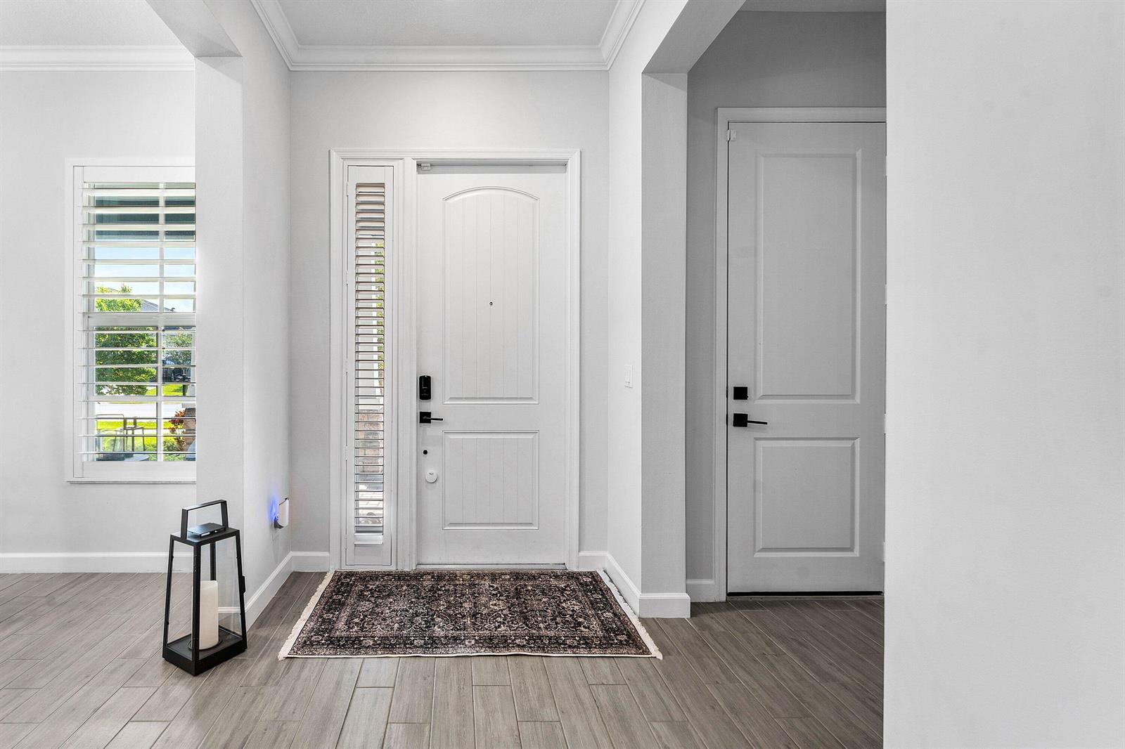 An entryway features a white front door with a sidelight, wood-look flooring, and a rug — 981 Castaway Court, Loxahatchee FL 33470, LOXAHATCHEE, FL