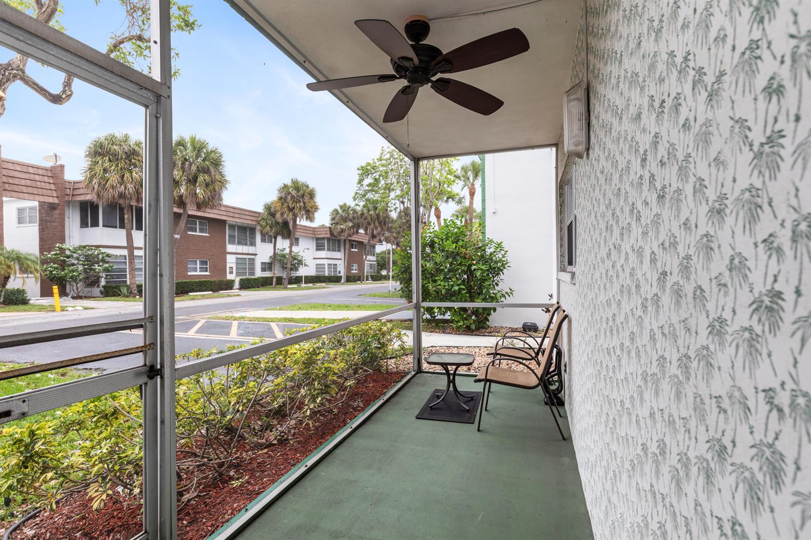 A screened-in patio features a ceiling fan, two chairs, a small table, and palm-patterned wallpaper — 2271 NW 48th Terrace # 111, Lauderhill FL 33313, LAUDERHILL, FL