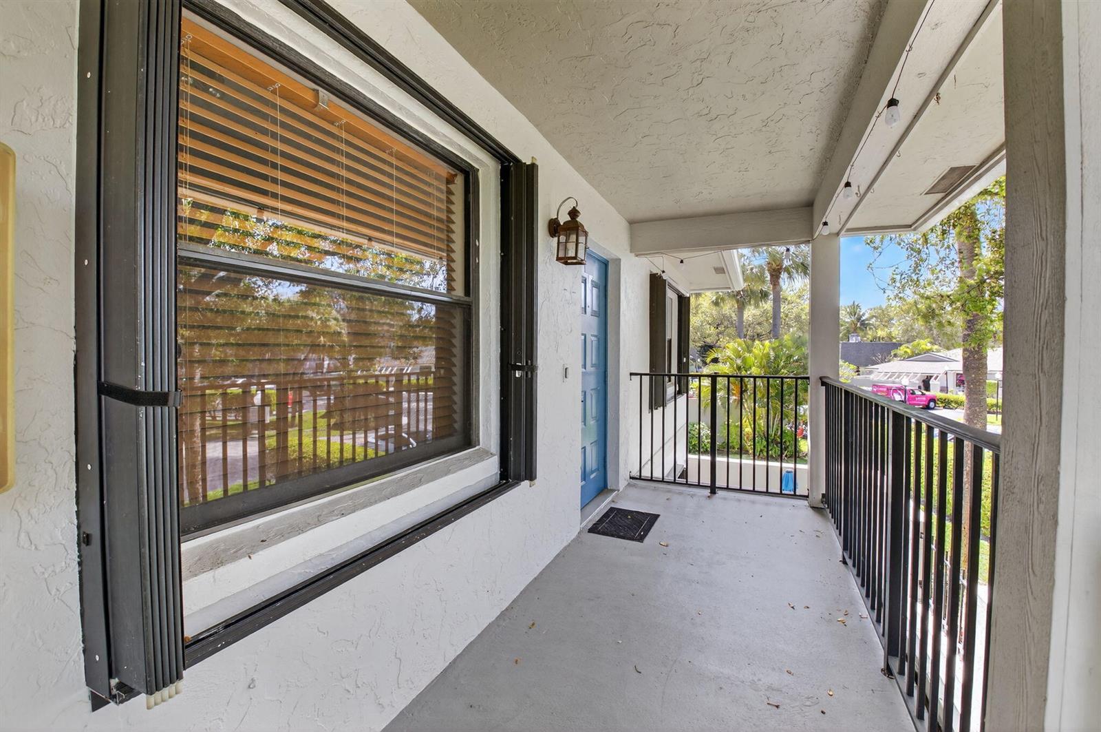 A covered balcony features a blue door, a large window with blinds, and black railings — 2911 SW 21st Terrace # 272b, Delray Beach FL 33445, DELRAY BEACH, FL