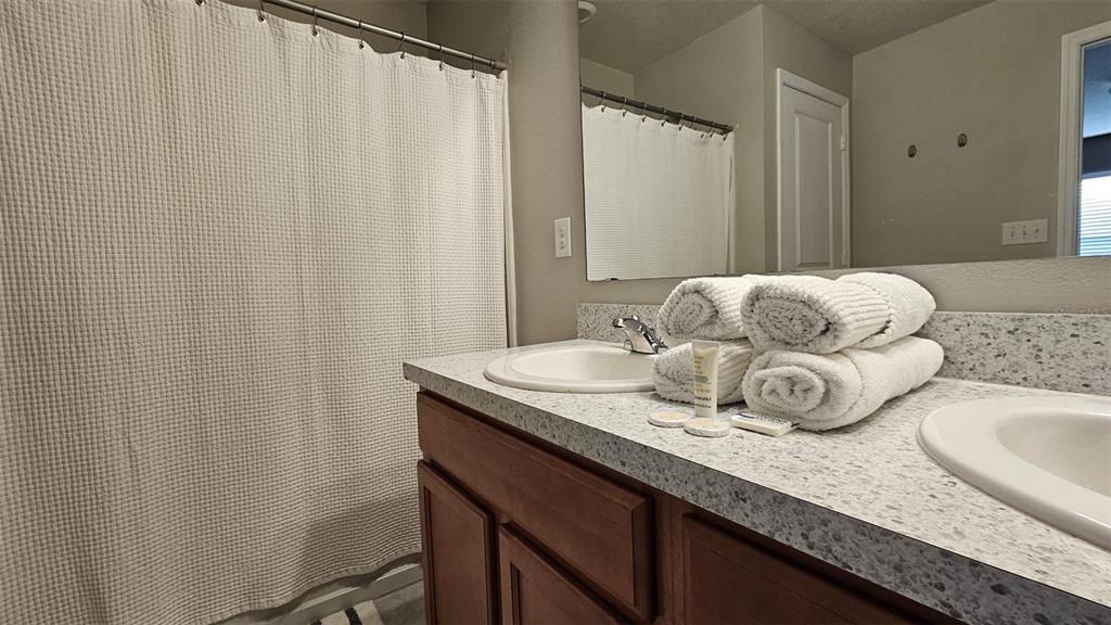 A bathroom features a double vanity with a speckled countertop, wood cabinets, and a shower — 308 LAKE LUCERNE WAY, WINTER HAVEN, FL