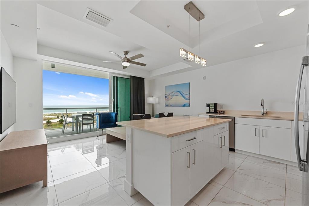 A modern kitchen with a white island and tile floors overlooks a balcony and ocean — 11500 GULF BOULEVARD UNIT 610, ST PETERSBURG, FL