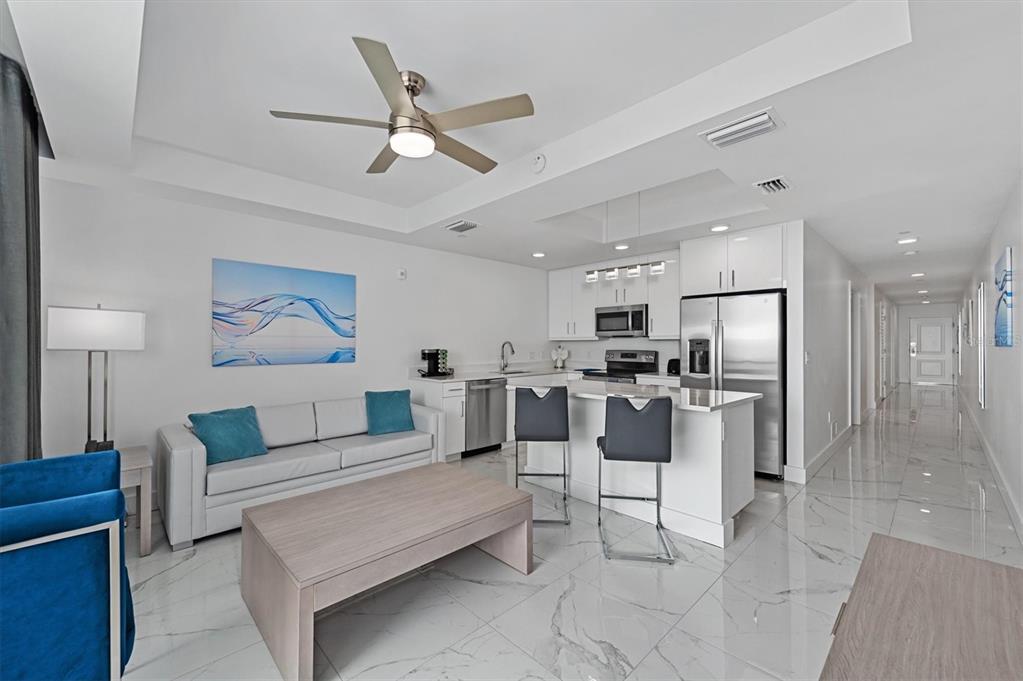A modern open-concept living room and kitchen featuring white cabinetry, stainless steel appliances, and tile — 11500 GULF BOULEVARD UNIT 610, ST PETERSBURG, FL