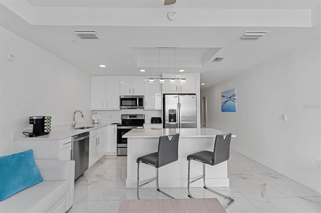 A modern kitchen features white cabinets, stainless steel appliances, a center island, and tiled floors — 11500 GULF BOULEVARD UNIT 610, ST PETERSBURG, FL