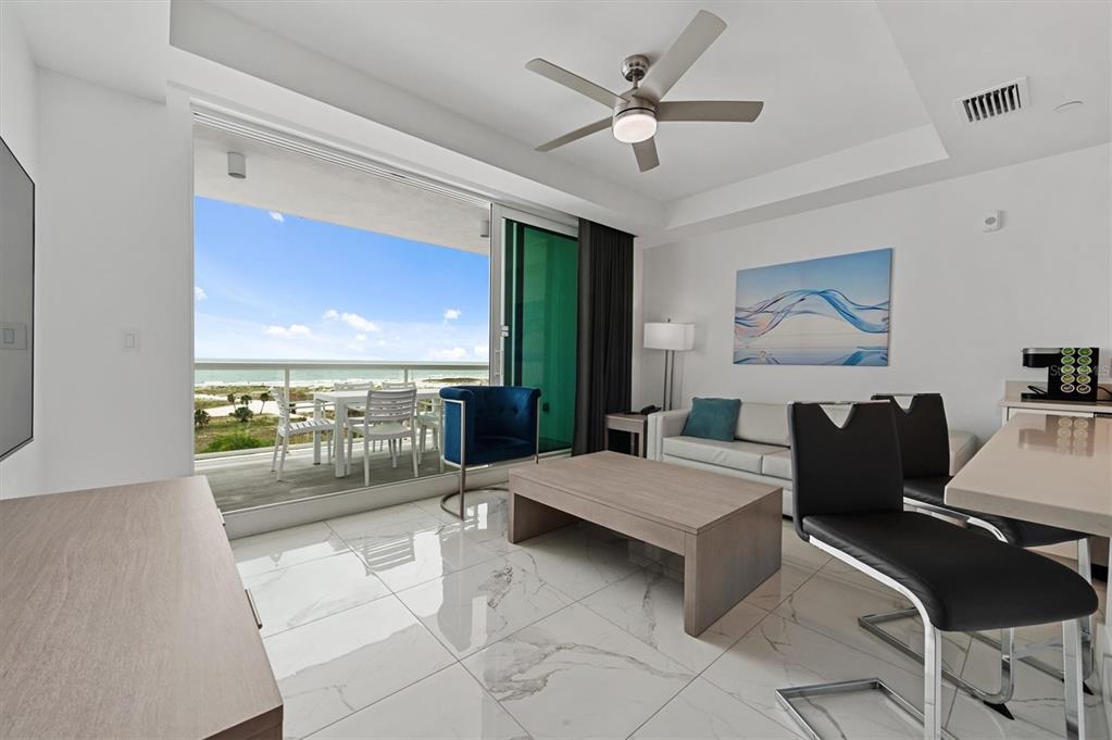 A modern living room features white marble floors, a ceiling fan, and a balcony overlooking the beach — 11500 GULF BOULEVARD UNIT 610, ST PETERSBURG, FL