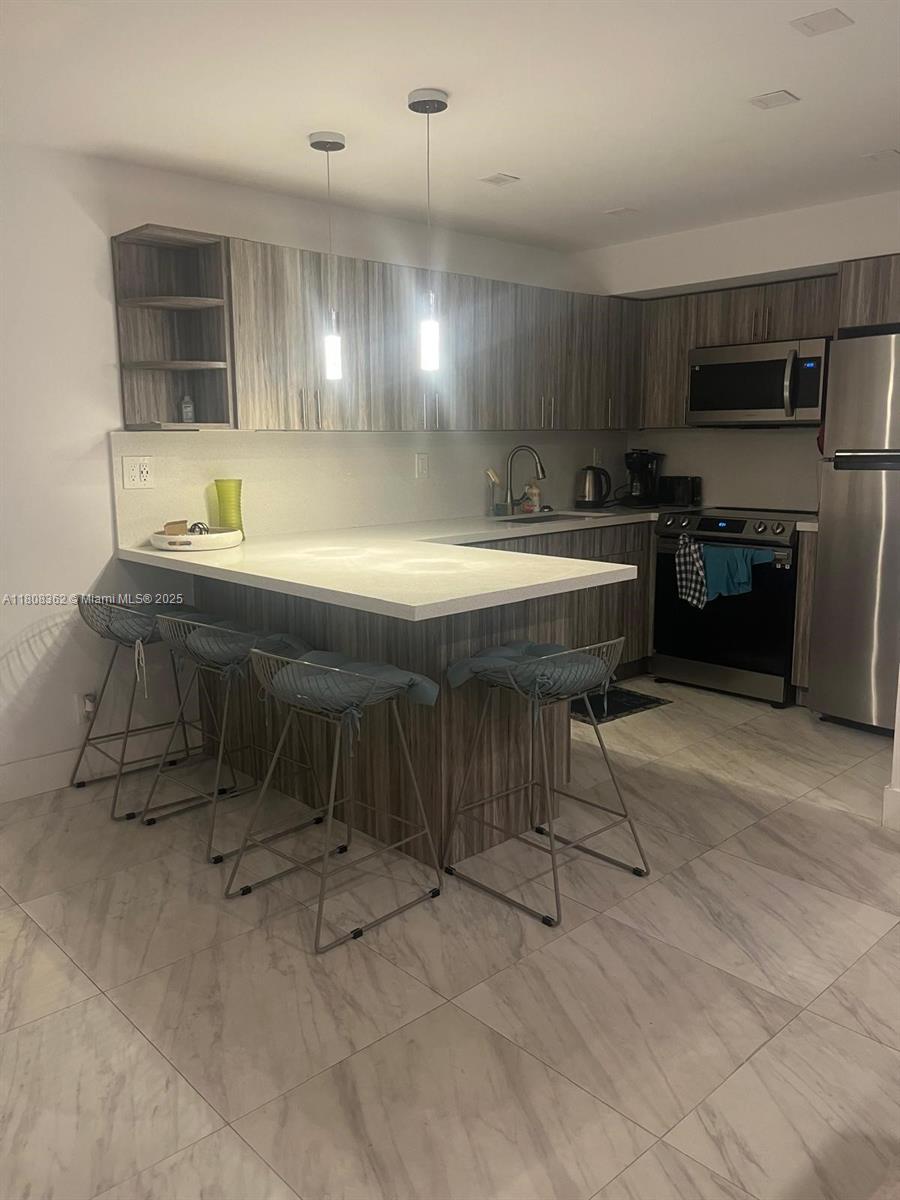 A modern kitchen features wood-grain cabinets, a white peninsula countertop, and four metal bar stools — 2145 Pierce St # 422, Hollywood FL 33020, HOLLYWOOD, FL