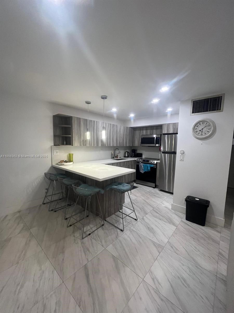 A modern kitchen features wood-grain cabinetry, a white countertop breakfast bar, and light marble flooring — 2145 Pierce St # 422, Hollywood FL 33020, HOLLYWOOD, FL