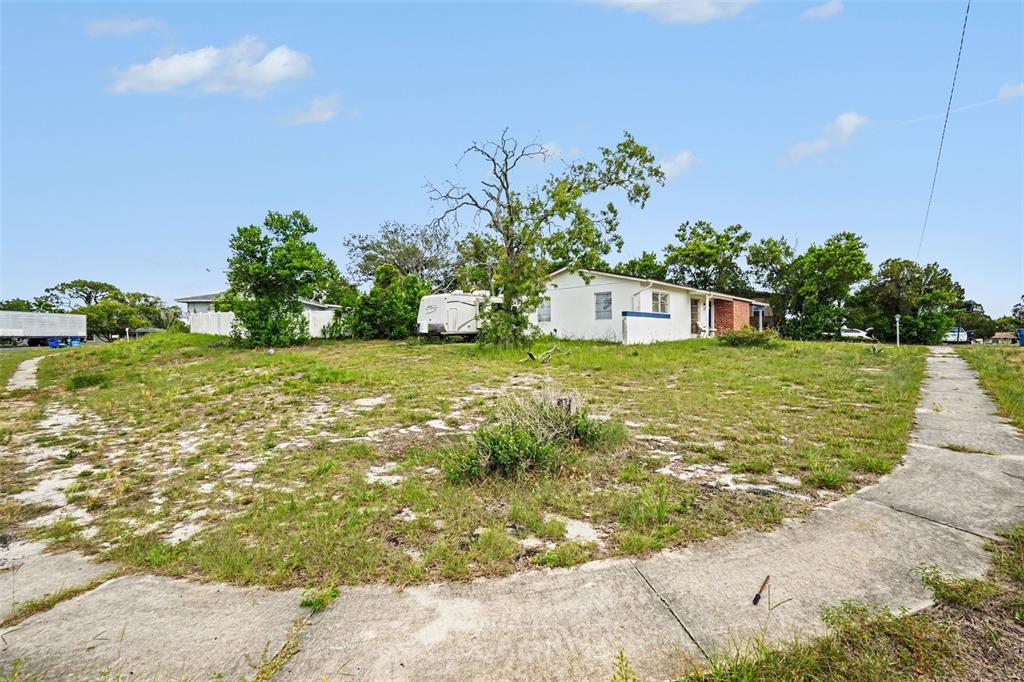 A white house with a camper trailer sits on a grassy lot with concrete sidewalks — 1096 MARLOW AVENUE, SPRING HILL, FL