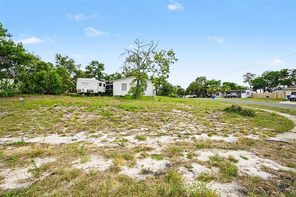 A vacant, sandy lot features a small white house and a parked recreational vehicle — 1096 MARLOW AVENUE, SPRING HILL, FL