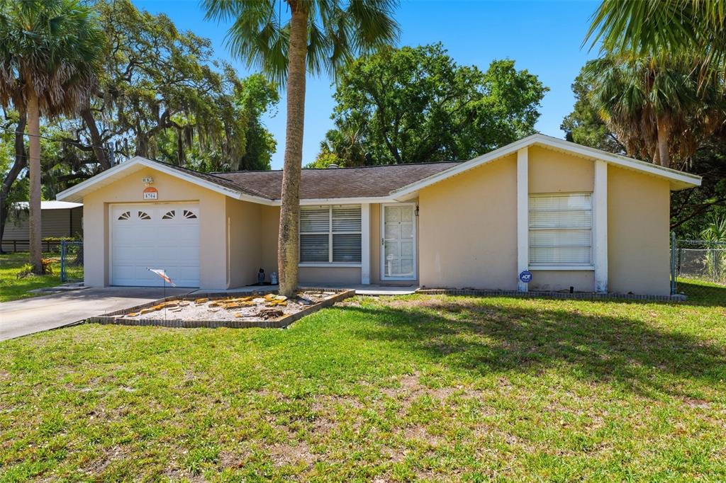 A single-story tan house with a garage, a front yard, and palm trees — 8704 LONG BOAT LANE, HUDSON, FL