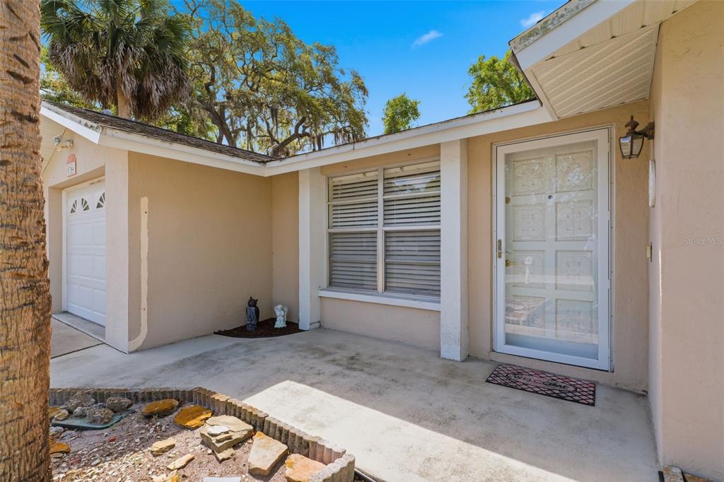 A beige house exterior features a front porch, a white garage door, and a storm door — 8704 LONG BOAT LANE, HUDSON, FL