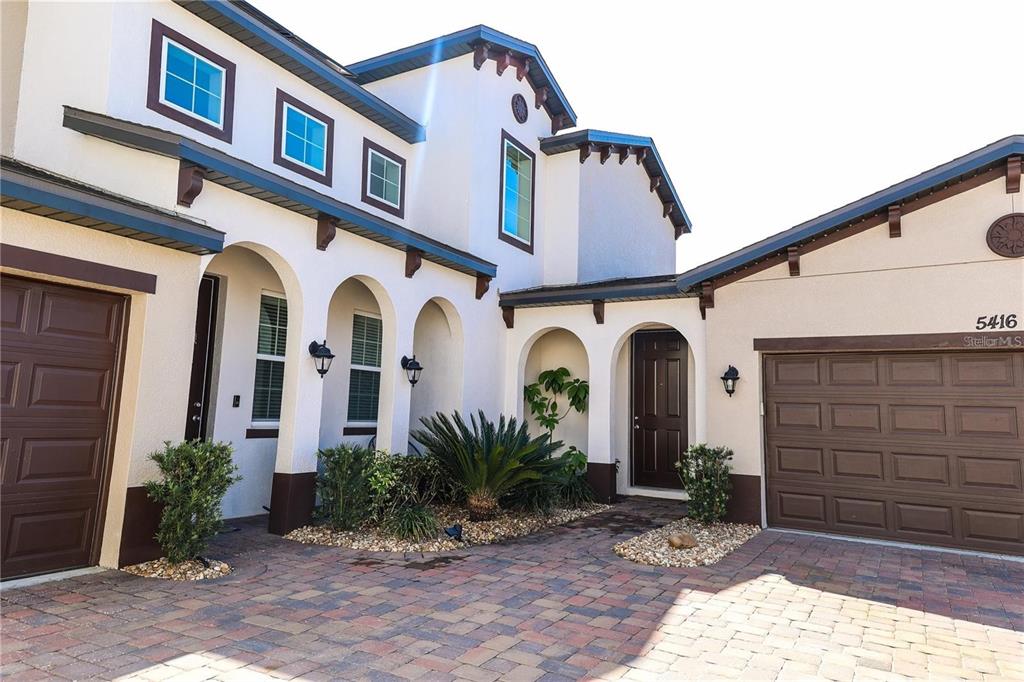 A two-story stucco house with a paver driveway, arched entryways, and two garage doors — 5416 CARRARA COURT, ST CLOUD, FL
