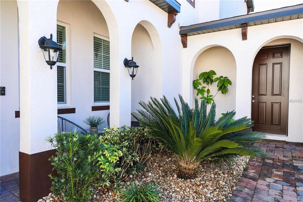 A white stucco house exterior features arched entryways, a brown front door, and landscaping — 5416 CARRARA COURT, ST CLOUD, FL