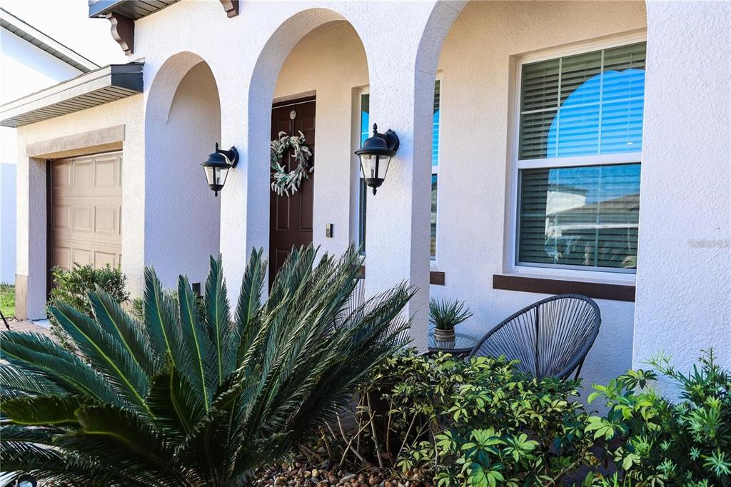 A front porch with arched entryways, a dark brown door, and a modern patio chair — 5416 CARRARA COURT, ST CLOUD, FL
