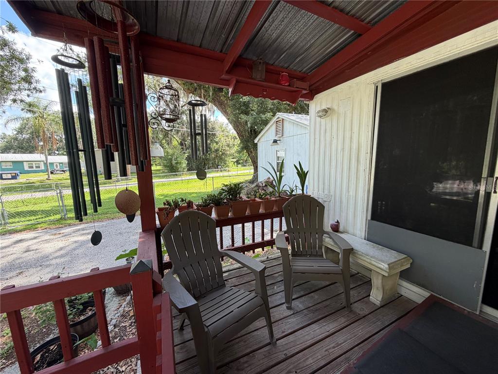 A covered wooden porch features two chairs, potted plants, and hanging wind chimes — 3315 CR 431N, LAKE PANASOFFKEE, FL