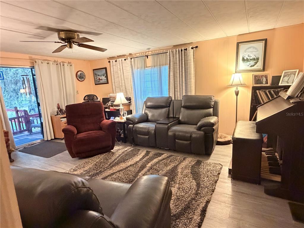 A living room features a brown loveseat, a red recliner, and a piano on wood-look flooring — 3315 CR 431N, LAKE PANASOFFKEE, FL