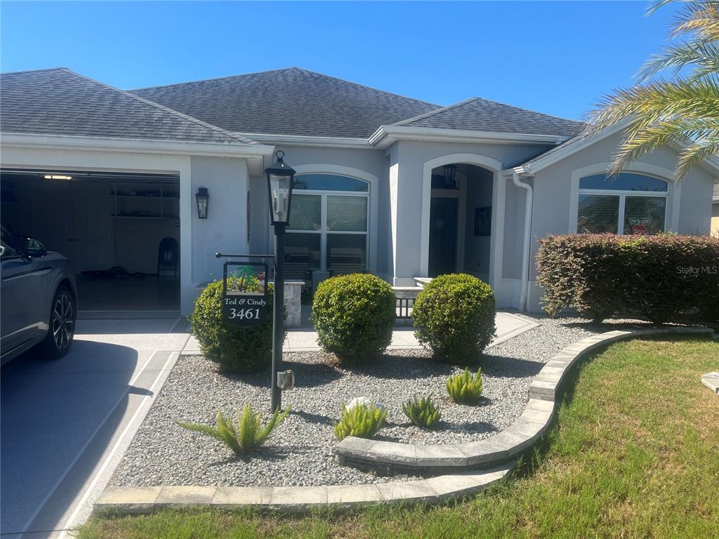 A single-story house features a gray exterior, a two-car garage, and a landscaped front yard — 3461 EARL WAY, THE VILLAGES, FL