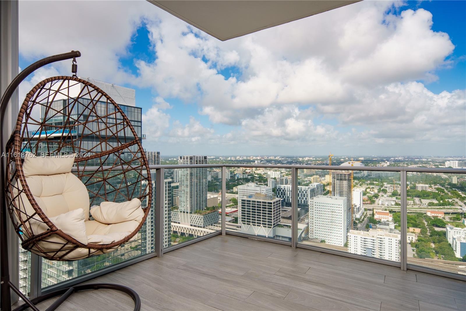 A high-rise balcony features a hanging egg chair and glass railings overlooking a city skyline — 851 NE 1st Ave # 4406, Miami FL 33132, MIAMI, FL