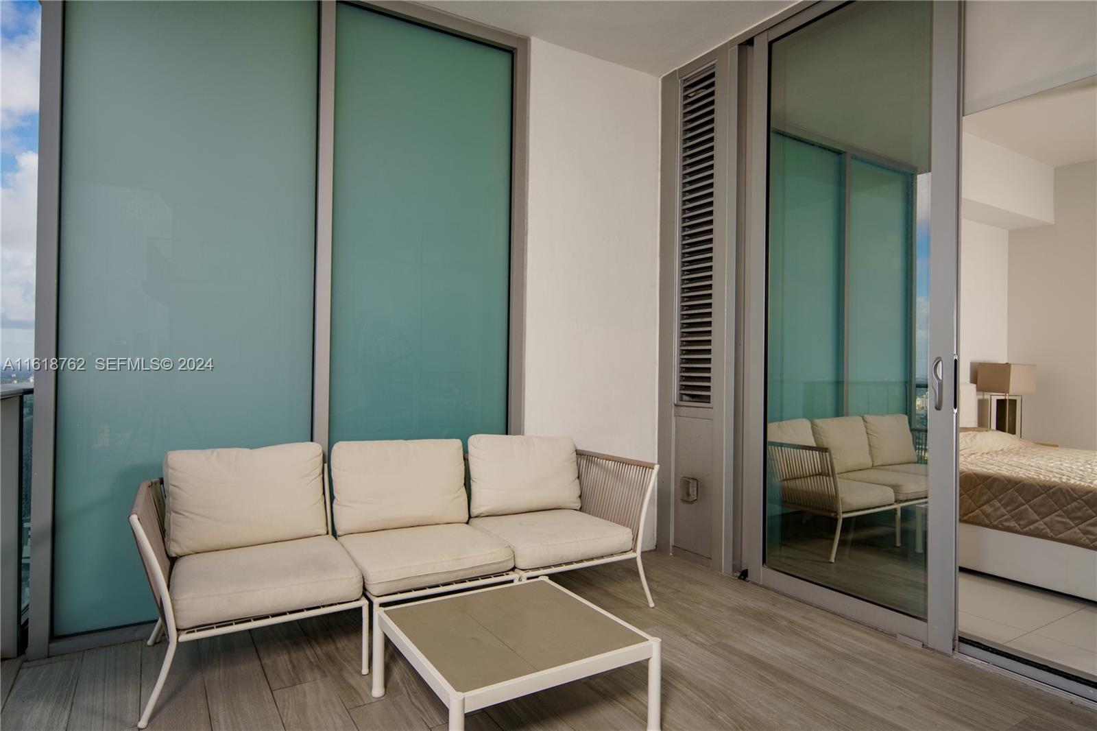 A balcony features a light-colored sofa, a small square table, and sliding glass doors — 851 NE 1st Ave # 4406, Miami FL 33132, MIAMI, FL